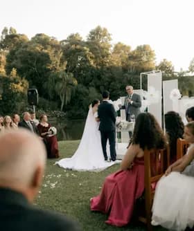 Outdoor wedding ceremony beside a lake, watched by seated guests