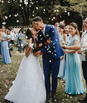 Newlyweds kissing while guests throw flower petals over them