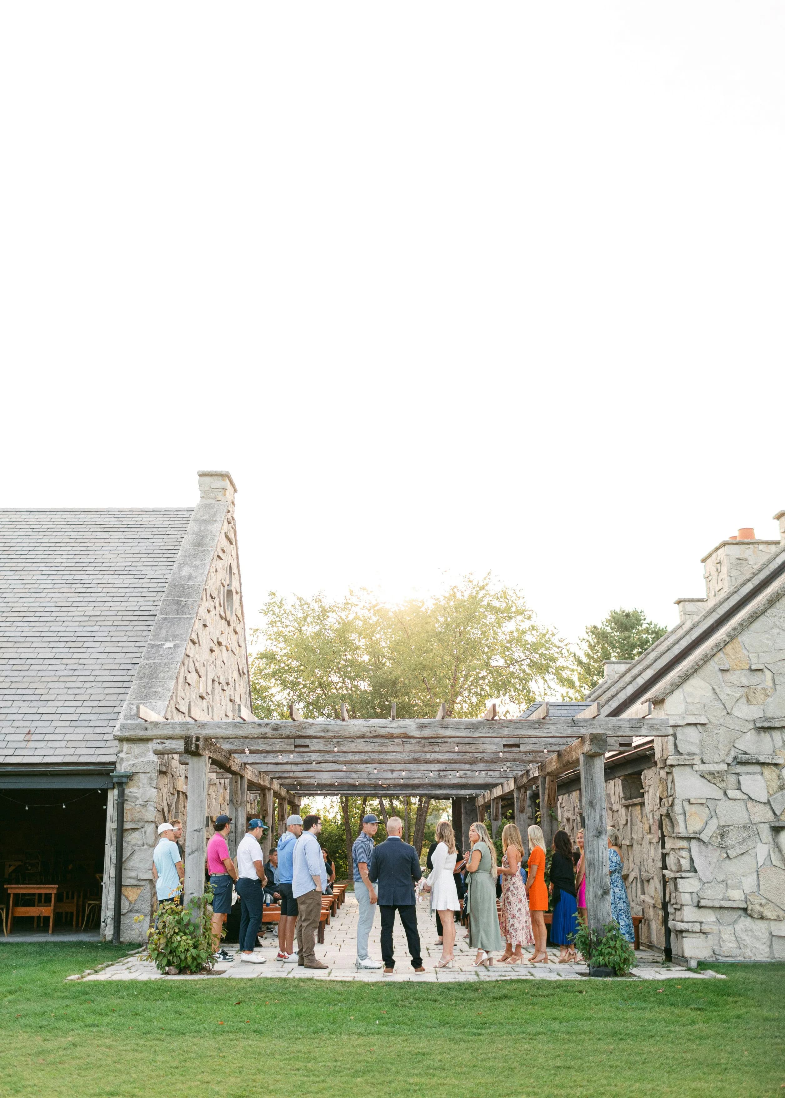 Guests gathered under a string-lit pergola at a stone venue at sunset